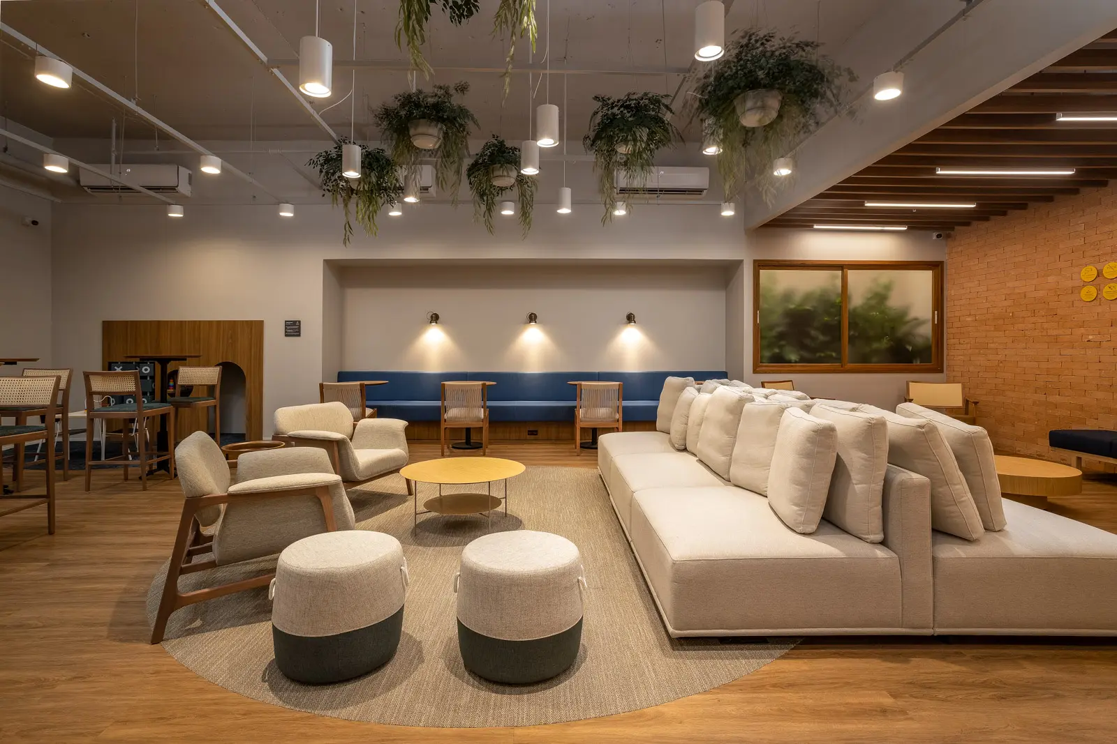 Lounge na Barra da Tijuca, com plantas suspensas, sofás claros e poltronas de madeira